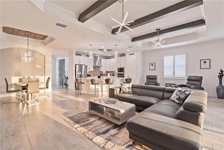 Open-concept living space featuring tray ceilings with exposed beams, recessed lighting, and large format tile flooring