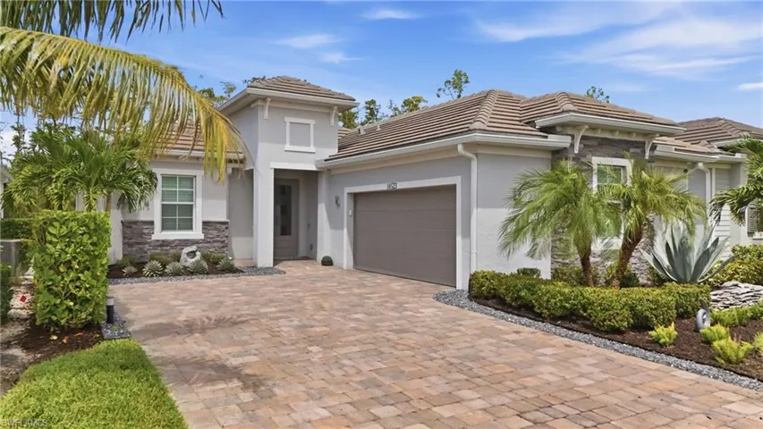 Stucco exterior with stone accents, tile roof, paver driveway, and an integrated garage