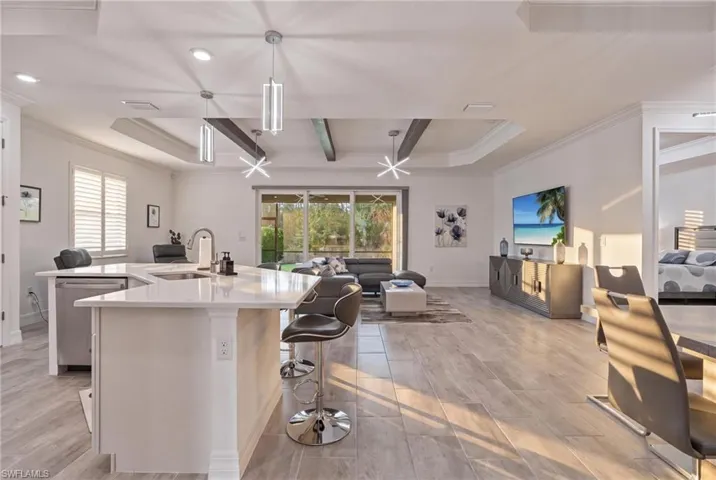 Open-concept living area with large format tile flooring and tray ceilings featuring exposed beams