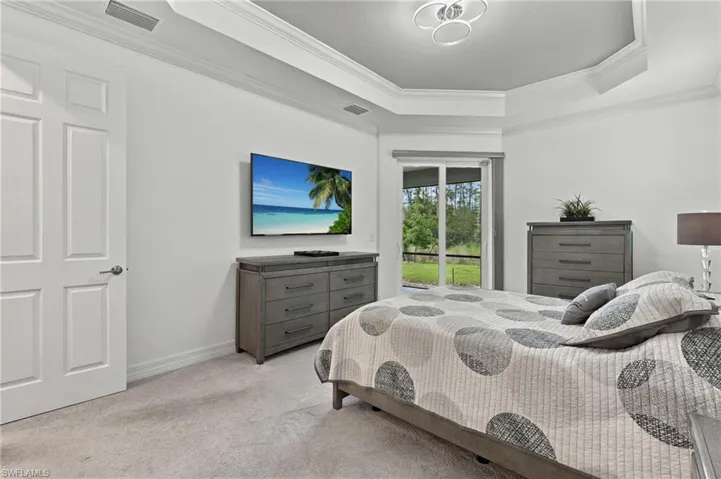 Tray ceiling with crown molding, wall-mounted television, sliding glass doors, and light-toned carpet flooring