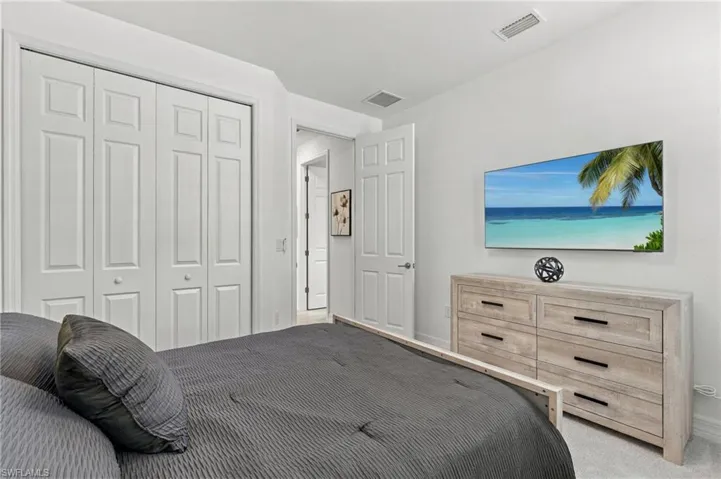 White paneled bi-fold closet doors, light-colored wood-finish dresser with black hardware, and wall-mounted television