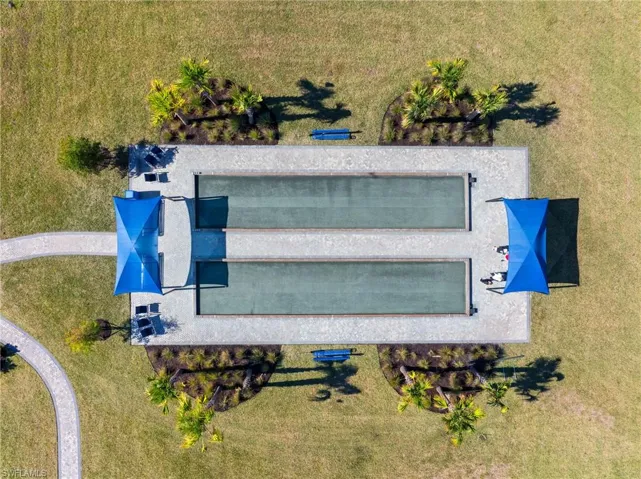 Two bocce ball courts with perimeter hardscaping, shade structures, curved paved pathways, and surrounding landscaped areas with mature plantings