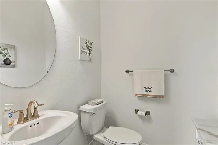 Pedestal sink with a brass-finish faucet, circular wall mirror, and white toilet