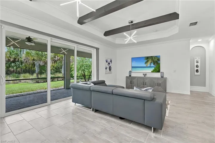 White tray ceiling with dark wood beams, contemporary pendant lighting, light-toned tile flooring, and large sliding glass doors opening to a screened outdoor area with a dark paver patio