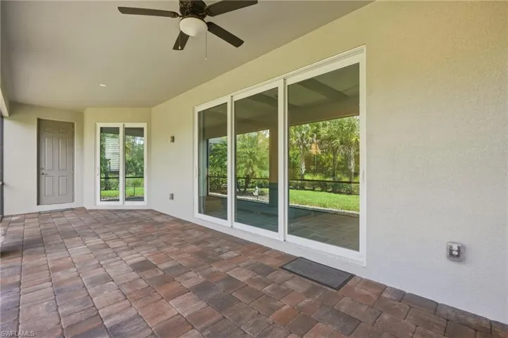Covered patio with paver flooring, multiple sliding glass doors, a ceiling fan with integrated lighting, and a paneled entry door