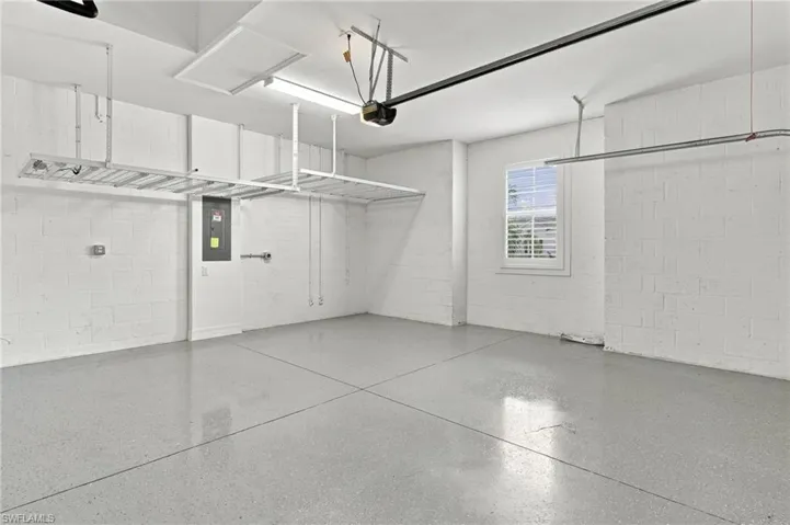 Concrete block walls, overhead storage racks, sealed concrete flooring, a single window, and exposed ceiling joists
