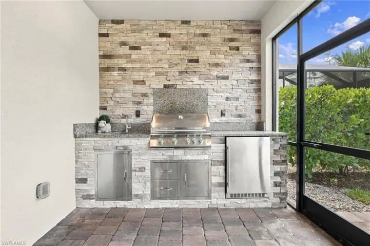 Outdoor kitchen featuring stacked stone, stainless steel appliances, granite countertops, and paver flooring