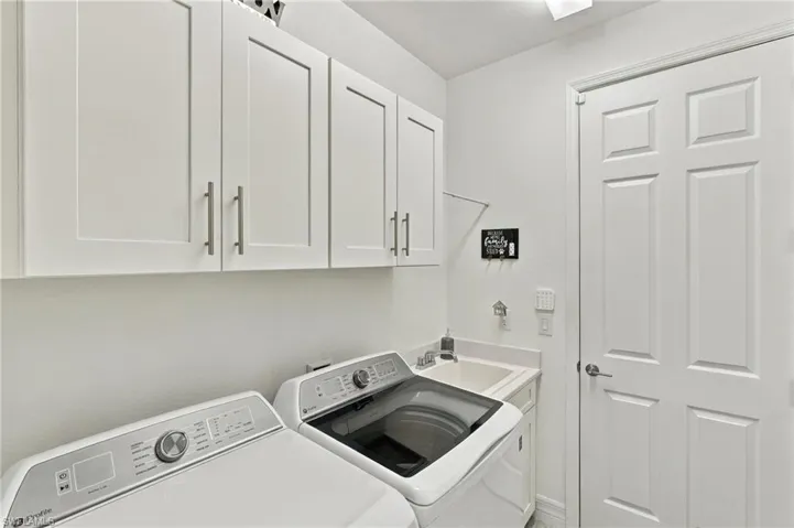 White shaker-style cabinetry with brushed nickel hardware, built-in utility sink, and white paneled door