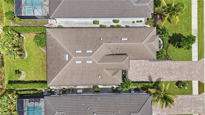 Tiled roof with multiple gables, extensive paved driveway, and manicured landscaping