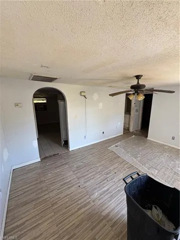 Unfurnished living room with arched walkways, ceiling fan, a textured ceiling, and wood finished floors