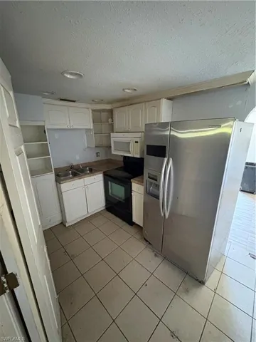Kitchen with fridge, electric stove, light tile patterned flooring, open shelves, and a textured ceiling