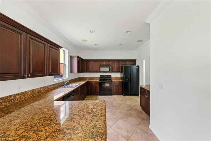 Kitchen featuring light tile patterned flooring, sink, stone counters, black appliances, and crown molding