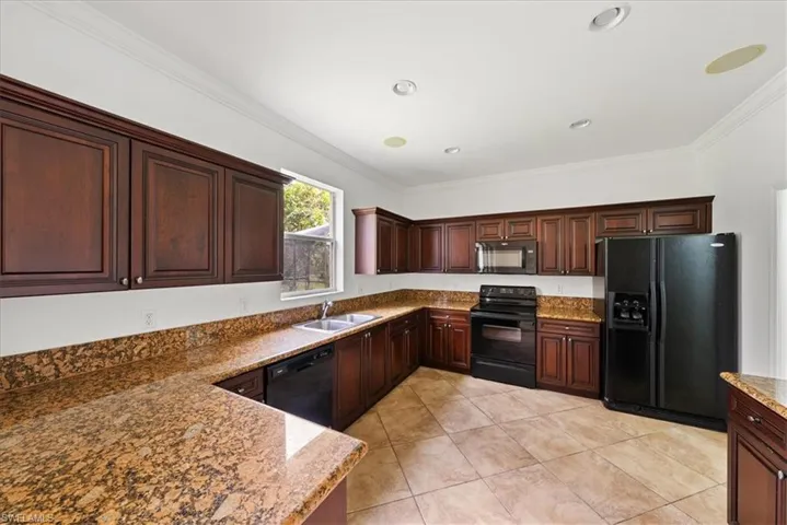 Kitchen featuring black appliances, crown molding, sink, and light stone countertops