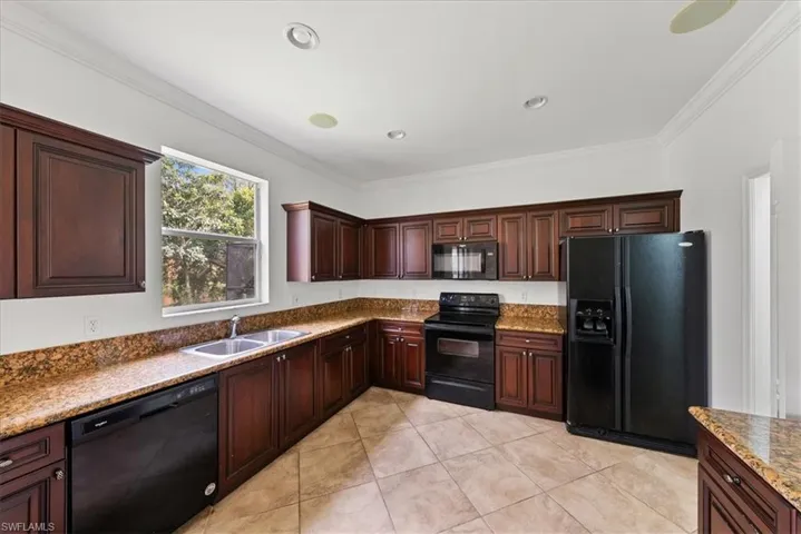 Kitchen featuring stone countertops, crown molding, sink, black appliances, and light tile patterned floors