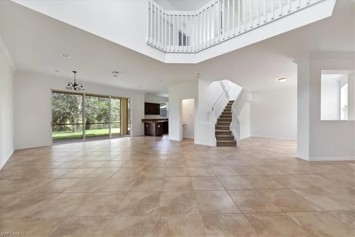 Unfurnished living room featuring ornamental molding, light tile patterned floors, a towering ceiling, and a chandelier