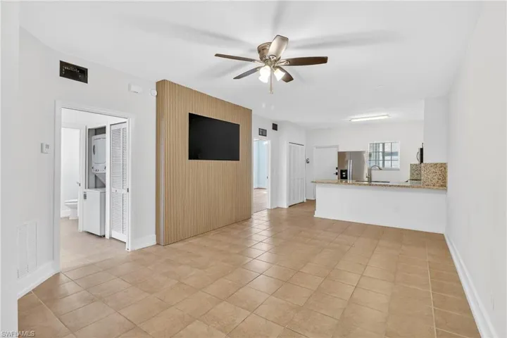 Unfurnished living room featuring stacked washer and dryer, ceiling fan, and light tile patterned flooring
