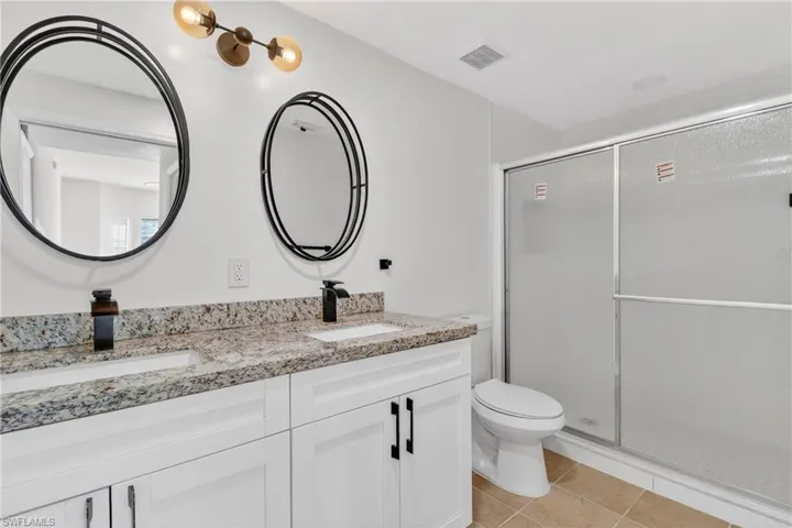 Full bath with double vanity, a shower stall, and light tile patterned floors