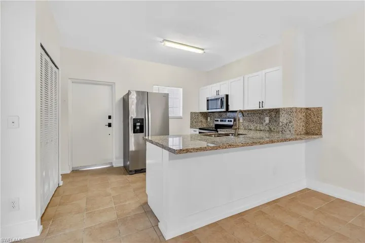 Kitchen featuring decorative backsplash, stainless steel appliances, white cabinets, light stone countertops, and a peninsula