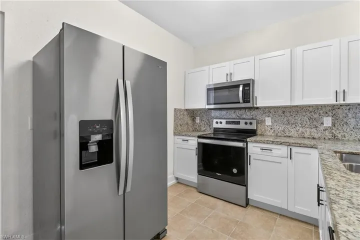 Kitchen featuring stainless steel appliances, white cabinetry, backsplash, light stone countertops, and light tile patterned flooring