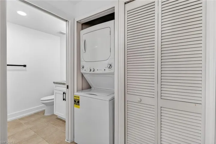 Laundry area with stacked washer / dryer and light tile patterned flooring