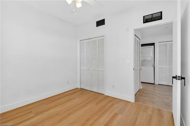 Unfurnished bedroom featuring stacked washer and clothes dryer, light wood-style flooring, a ceiling fan, and multiple closets