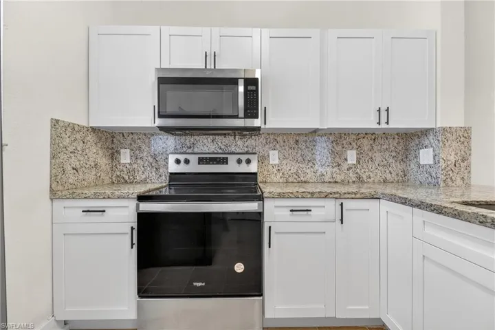 Kitchen with stainless steel appliances, white cabinetry, and light stone counters