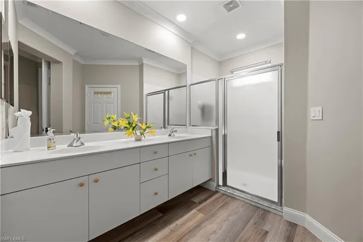 Bathroom with vanity, wood-type flooring, a shower with door, and crown molding