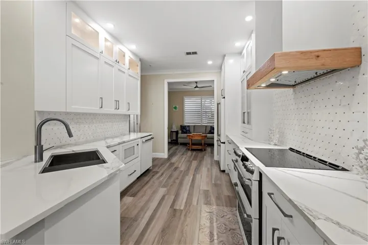 Kitchen featuring white cabinets, sink, custom range hood, crown molding, and white appliances