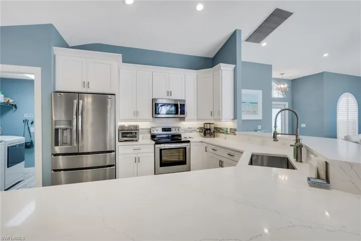 Kitchen featuring stainless steel appliances, white cabinetry, light stone countertops, a chandelier, and vaulted ceiling