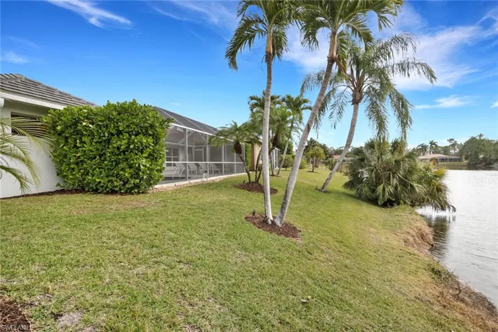 View of green lawn featuring a sunroom, a water view, and glass enclosure
