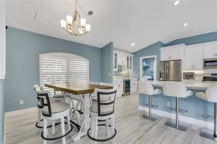 Dining space featuring lofted ceiling, light wood finished floors, wine cooler, and hanging lights