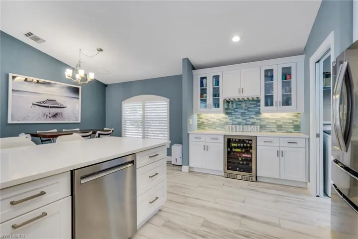 Kitchen featuring glass insert cabinets, white cabinets, stainless steel appliances, beverage cooler, and lofted ceiling