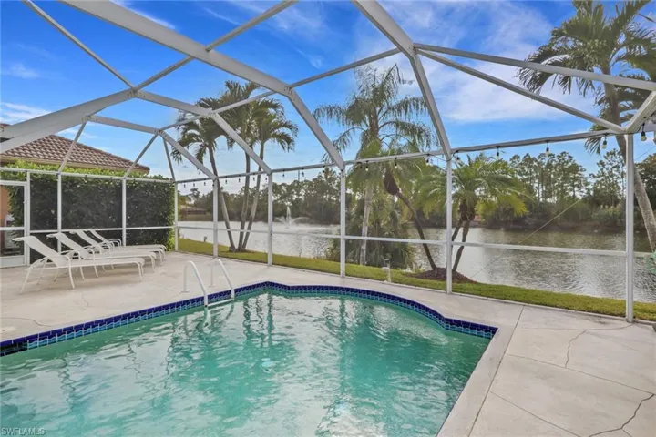 Outdoor pool with glass enclosure, a sunroom, a water view, and a patio area