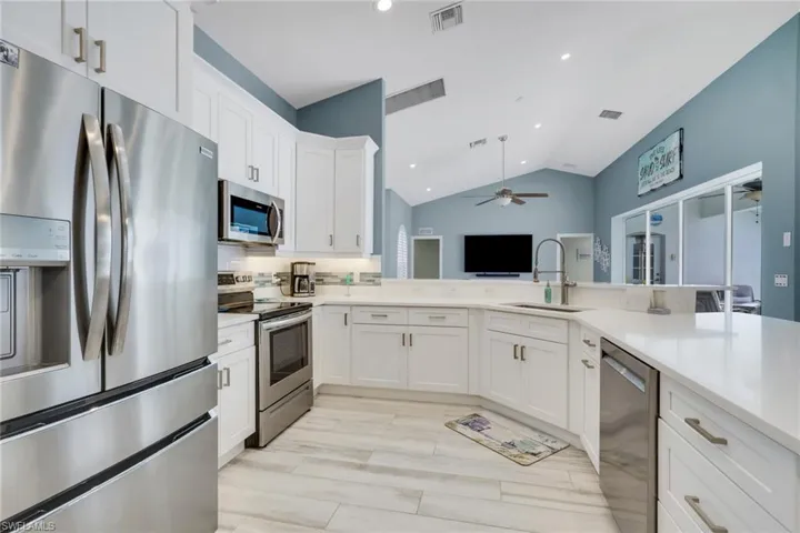 Kitchen featuring stainless steel appliances, lofted ceiling, white cabinetry, recessed lighting, and ceiling fan