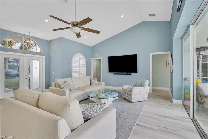 Living room with ceiling fan, light wood-style flooring, vaulted ceiling, french doors, and a chandelier
