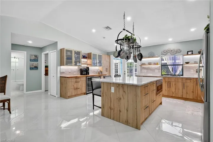 Kitchen featuring open shelves, lofted ceiling, a breakfast bar area, glass insert cabinets, and a center island