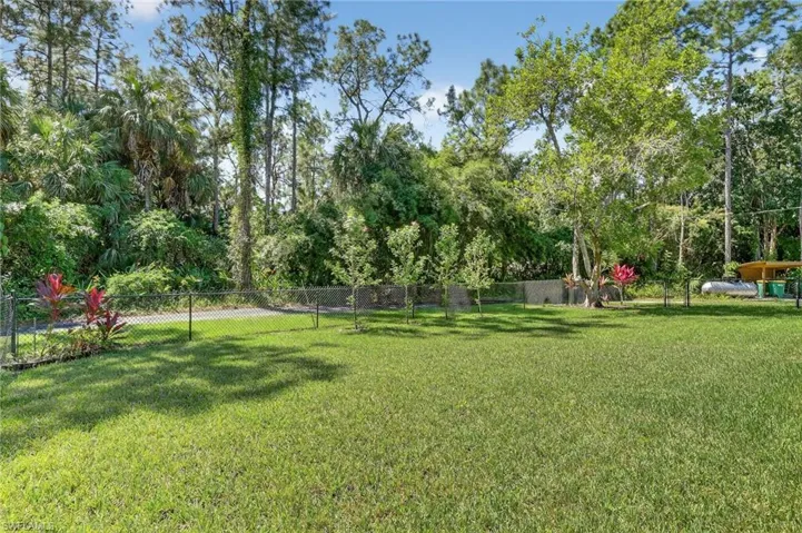 Side fenced yard with sprinkler system, featuring view of beautiful Hibiscus trees
