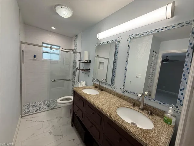 Master bath with double vanity, granite counters, light marble flooring, and shower with glass door.