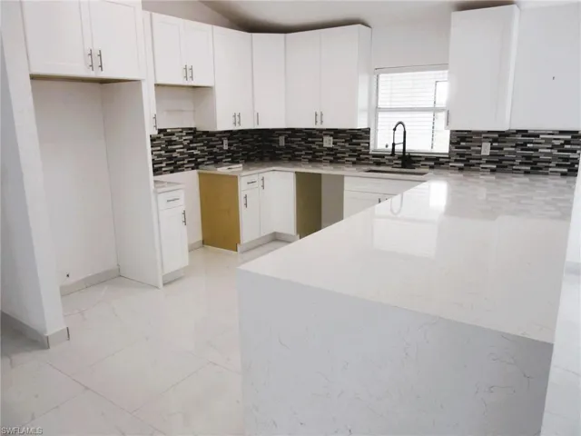 Kitchen featuring light stone countertops, a peninsula, white cabinetry, light marble finish floors, and backsplash