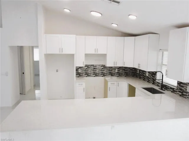 Kitchen with a peninsula, lofted ceiling, light stone countertops, white cabinets, and tasteful backsplash