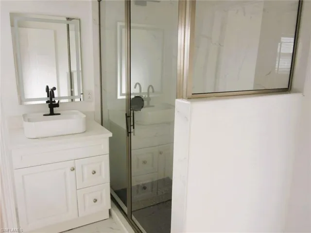 Full bath with vanity, a marble finish shower, and light marble finish flooring