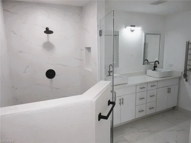 Full bath featuring a marble finish shower, double vanity, light marble finish floors, and a towel warming rack