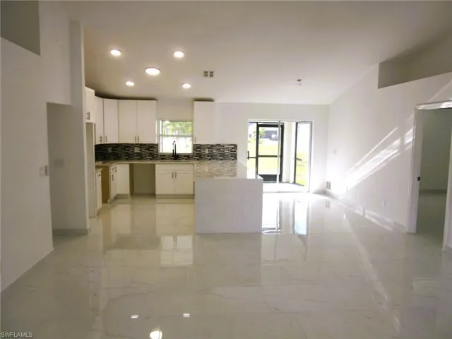 Kitchen featuring white cabinetry, light marble finish floors, tasteful backsplash, light stone countertops, and recessed lighting