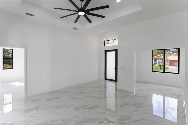 Empty room with a tray ceiling, plenty of natural light, light marble finish floors, a high ceiling, and recessed lighting