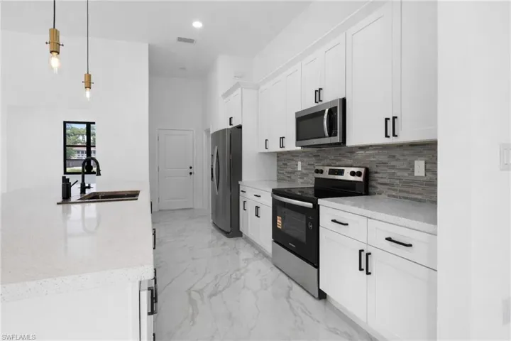 Kitchen with stainless steel appliances, white cabinets, hanging light fixtures, and light stone counters