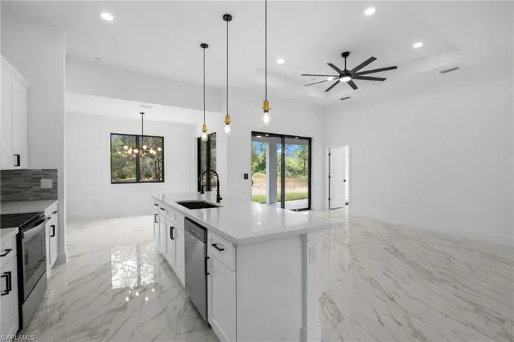 Kitchen featuring stainless steel appliances, a kitchen island with sink, a chandelier, white cabinets, and light stone countertops