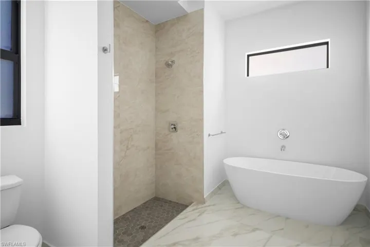 Full bathroom featuring a tile shower, a freestanding tub, and marble finish floors
