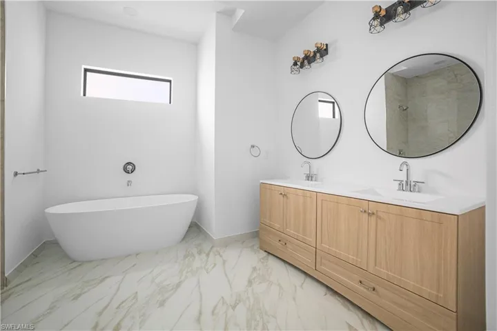 Full bath featuring light marble finish floors, double vanity, a soaking tub, and a shower