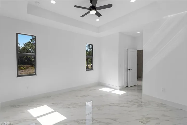 Empty room with a raised ceiling, light marble finish flooring, recessed lighting, and a ceiling fan