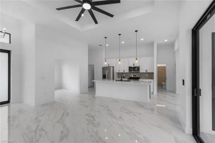 Kitchen with a kitchen island with sink, white cabinets, open floor plan, stainless steel appliances, and a tray ceiling